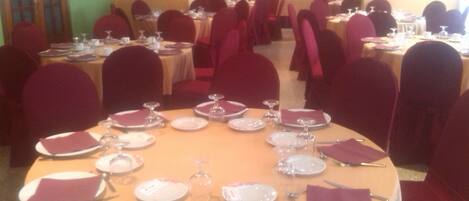 A formal dining room with round tables set for multiple guests, each table featuring white plates, cutlery, and wine glasses.