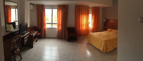 A hotel room with a bed, a desk with a chair, a television, and a window with curtains.