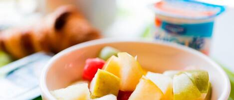 Un cuenco de fruta, una taza y un recipiente con yogur sobre una mesa.