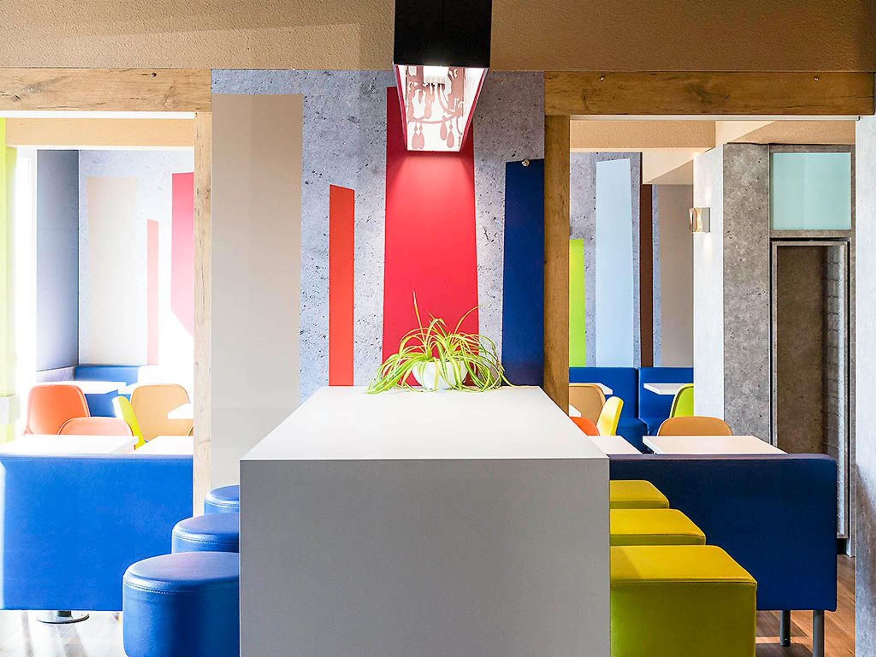 Un intérieur moderne avec une table blanche au centre, des sièges aux couleurs vives et un arrangement floral en guise de décoration.
