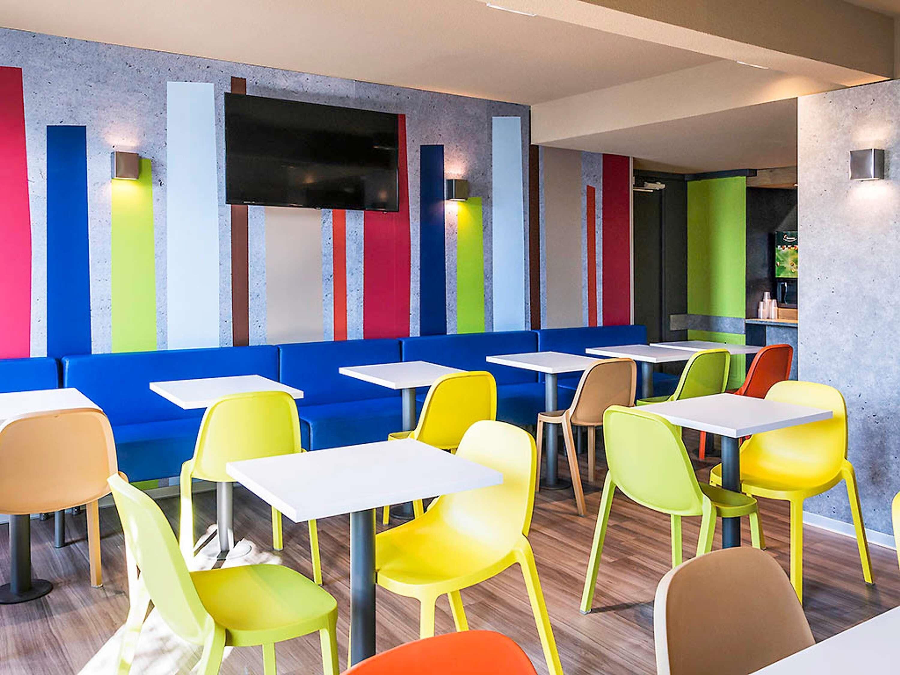 Un interior de restaurante moderno con asientos coloridos, una televisión de pantalla plana y una zona de bar.