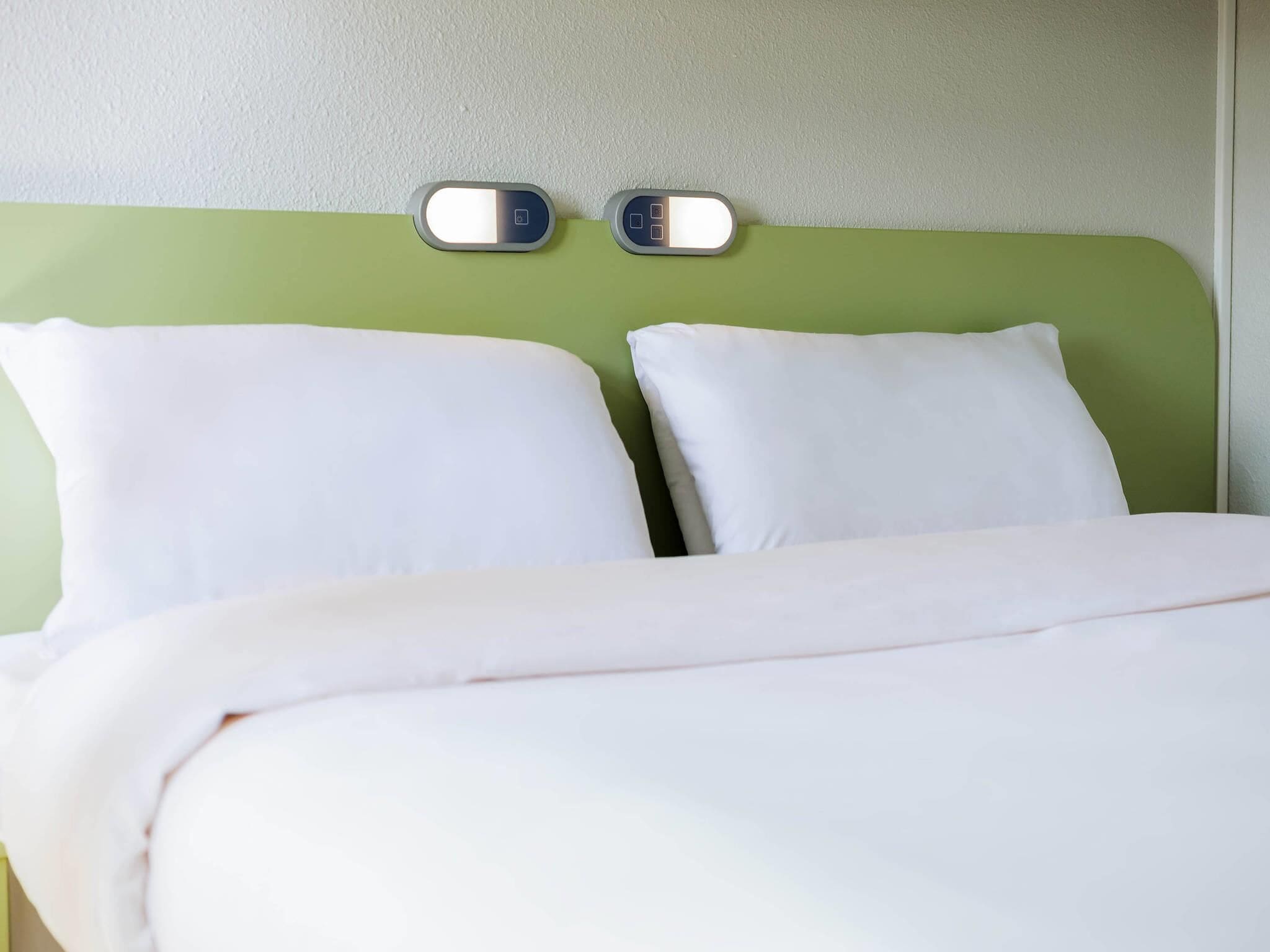 Una cama con dos almohadas blancas y un cabecero verde.