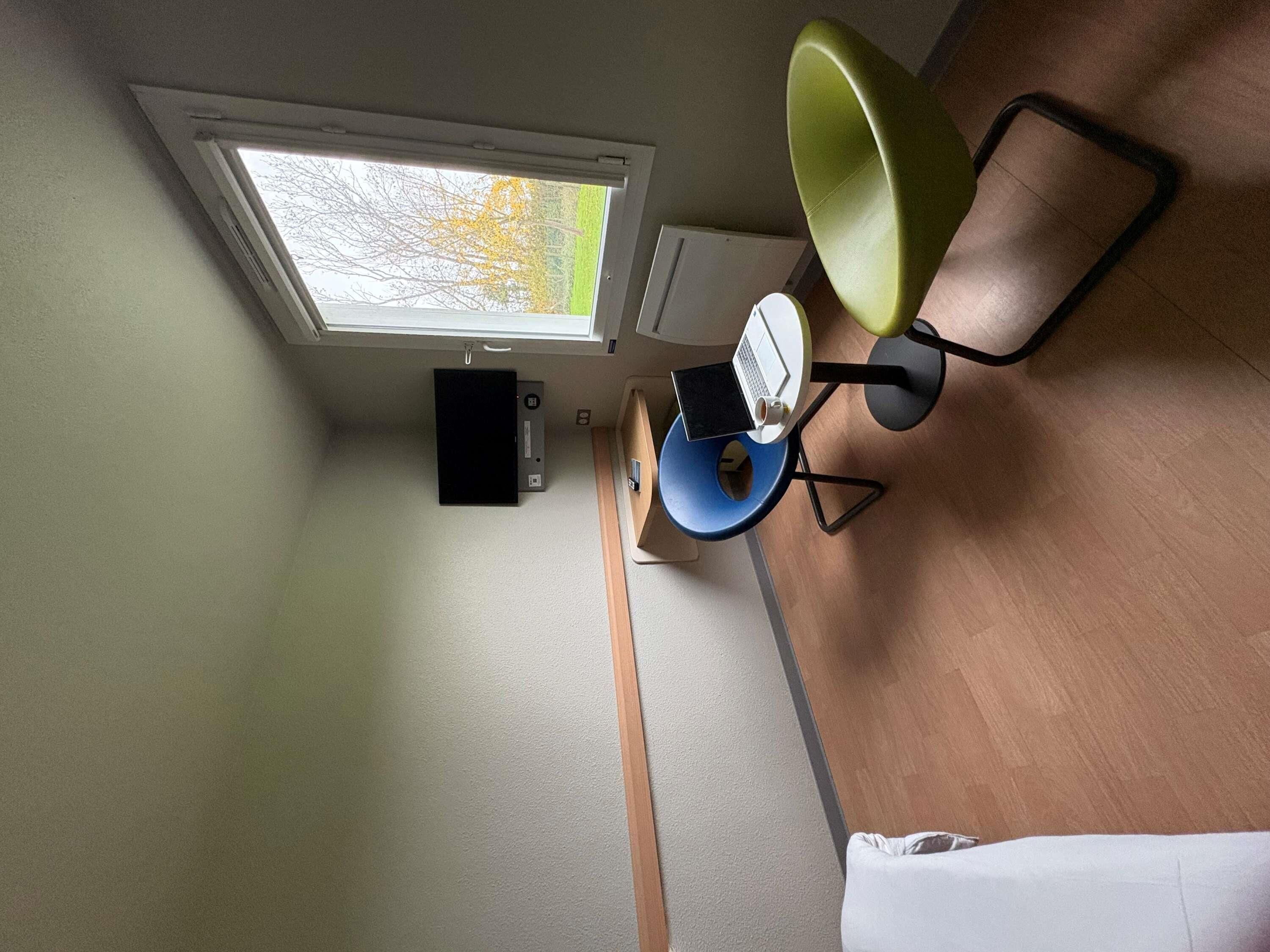 Una habitación con tragaluz, un escritorio con una computadora portátil, una silla y una cama.
