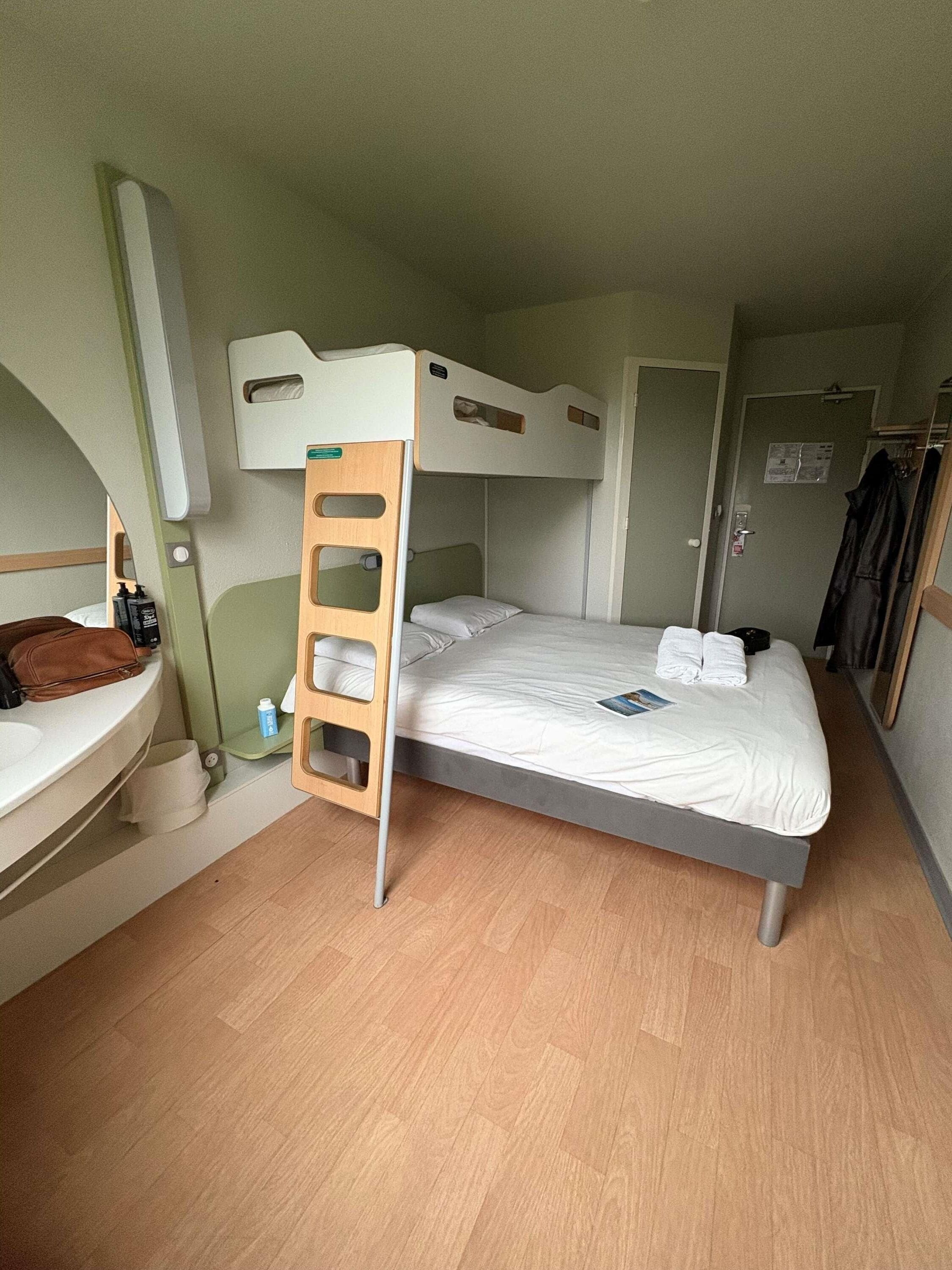 A bunk bed room with a wooden ladder, a small bedside table, a mirror, and a door.