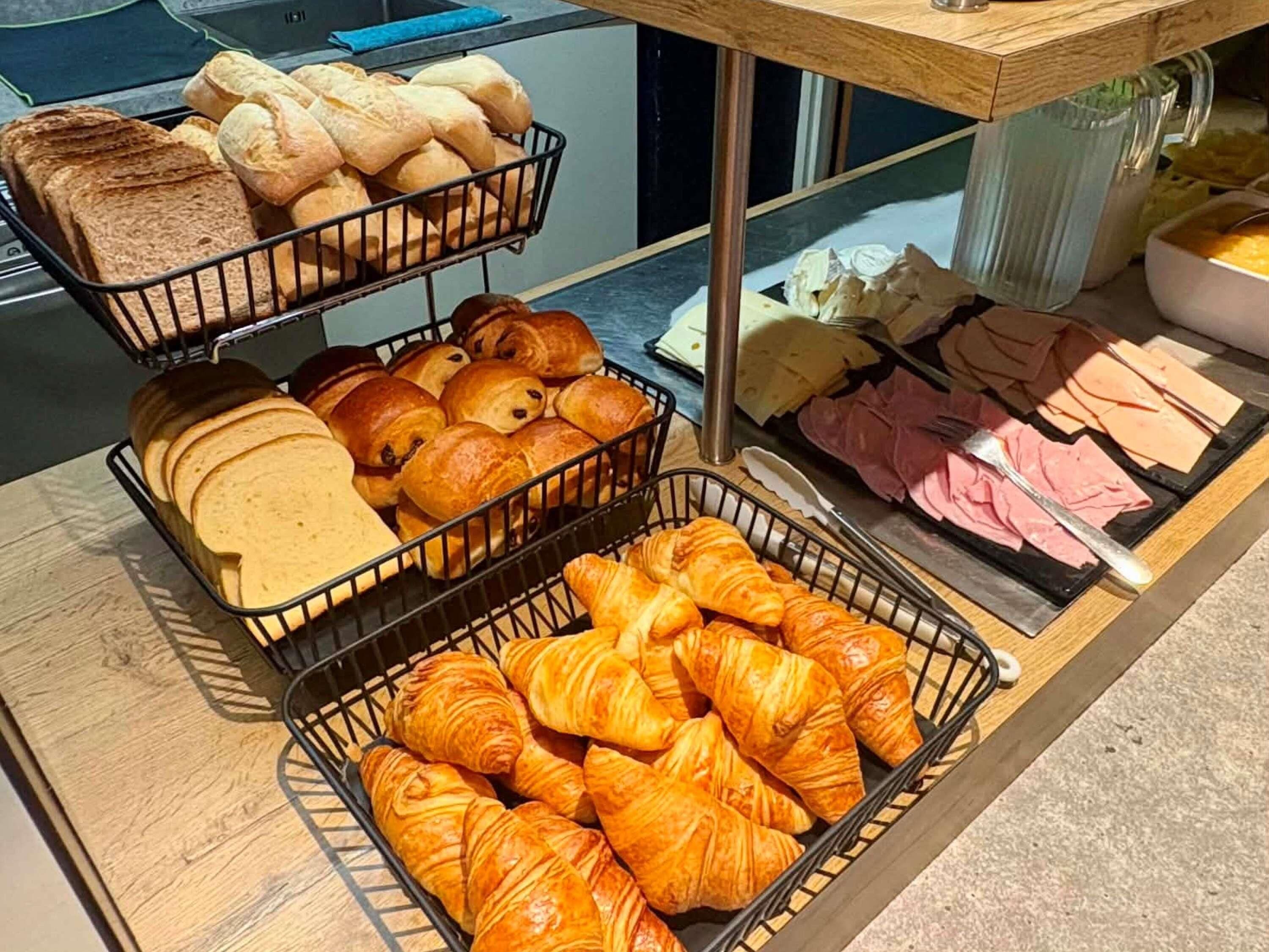 A breakfast buffet with bread, croissants, and various meats.