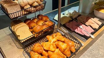A breakfast buffet with bread, croissants, and various meats.