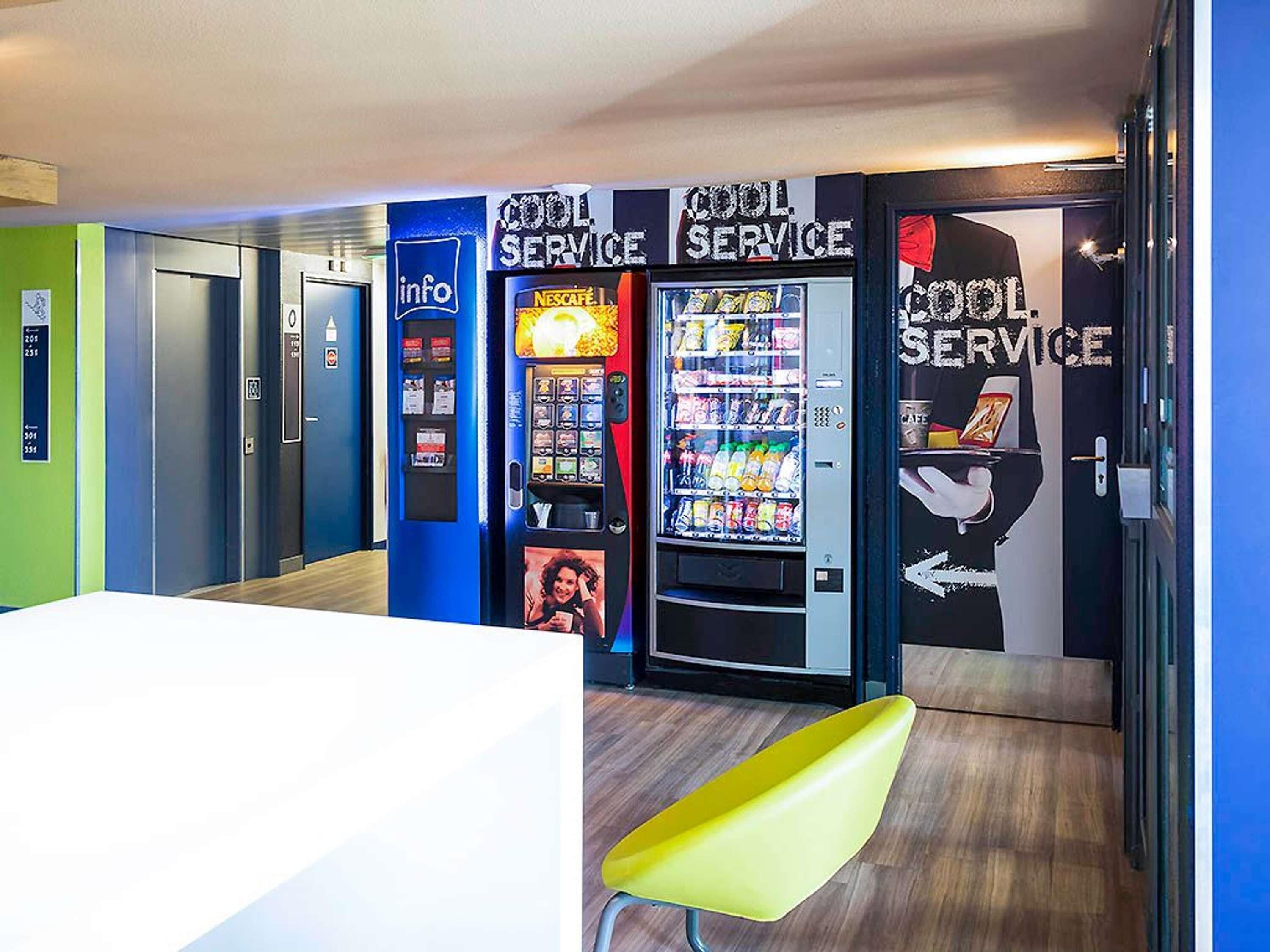 Un vestíbulo de hotel con máquinas expendedoras, una silla amarilla y una puerta con un cartel que dice 'Cool Service'.