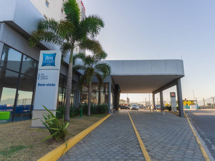 A modern hotel entrance with a covered walkway, palm trees, and a clear sky.