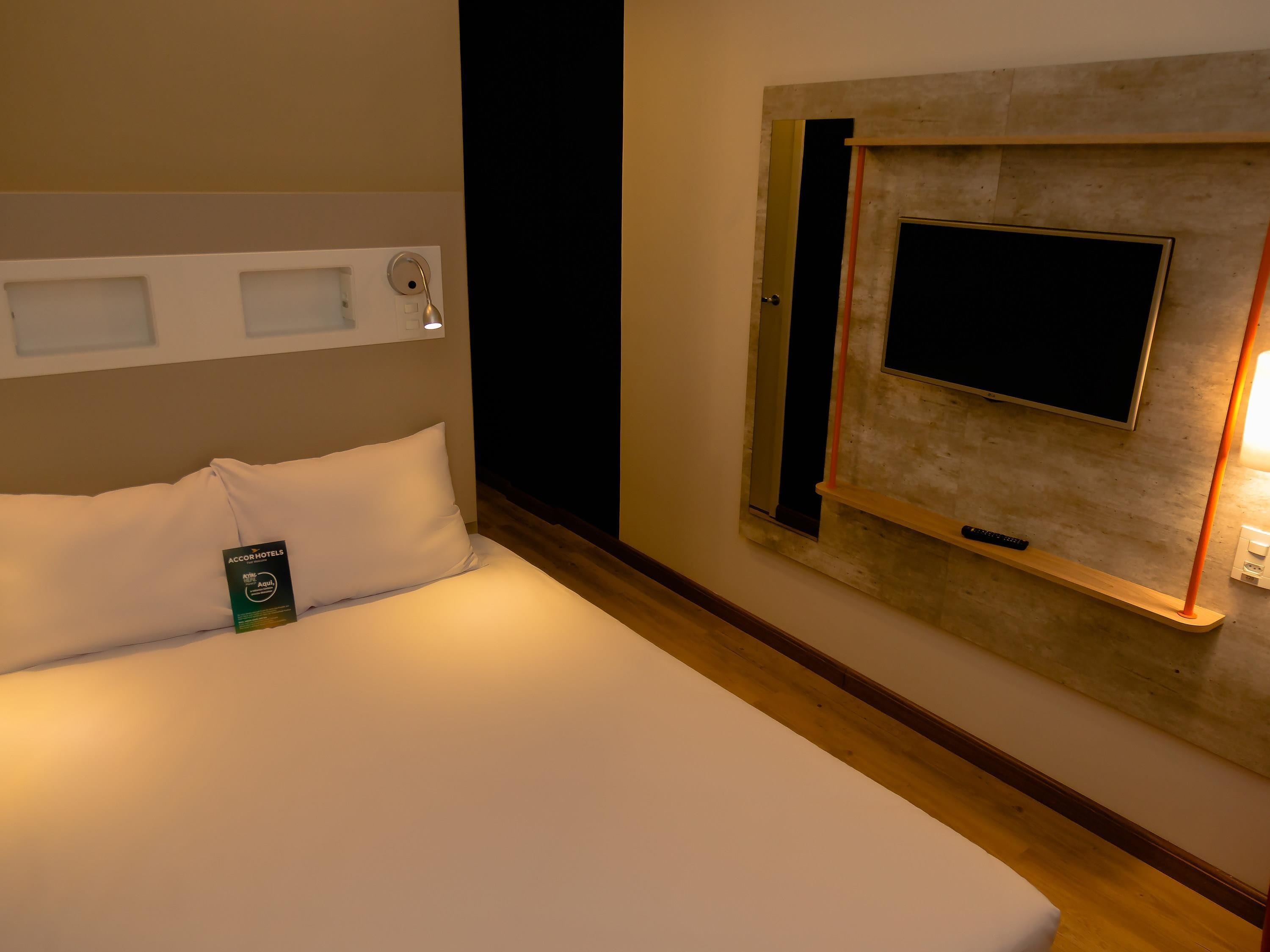 A hotel room with a bed, a wall-mounted TV, and a bedside table.