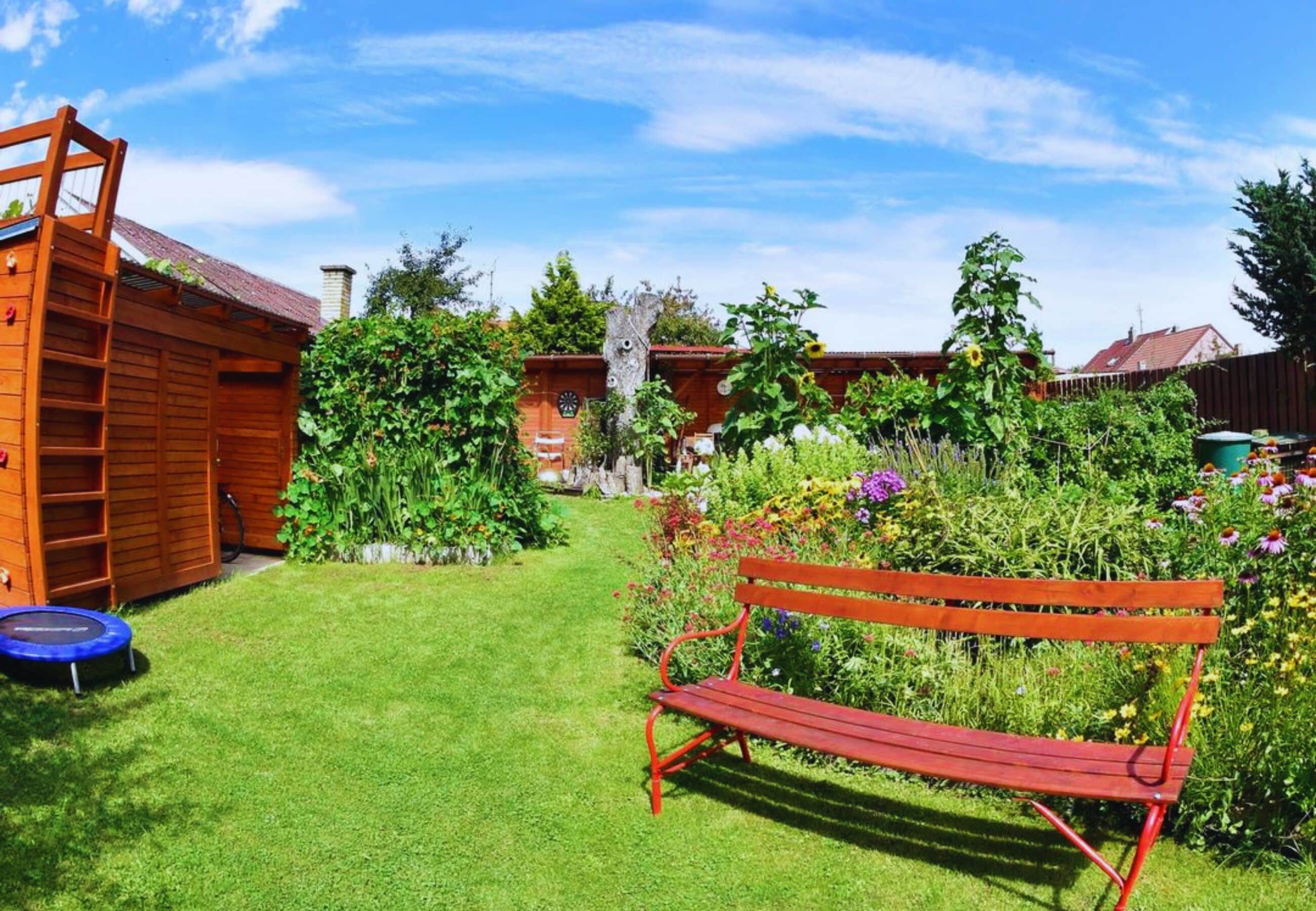 Een houten bankje in een tuin met een houten constructie en een trampoline.
