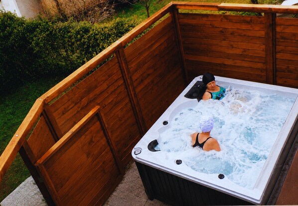 Un jacuzzi con cubierta de madera, rodeado de vegetación.