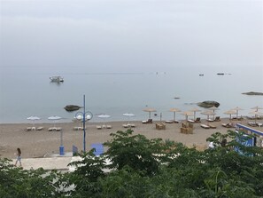Een strand met ligstoelen en parasols, een boot op het water en een rotsachtige richel.