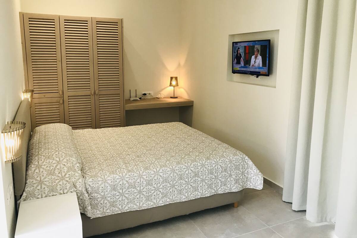 A bedroom with a bed, a nightstand, a lamp, a TV, and a wardrobe.