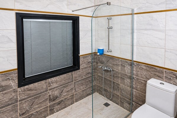 Un baño con ducha de vidrio, inodoro y ventana con persianas.