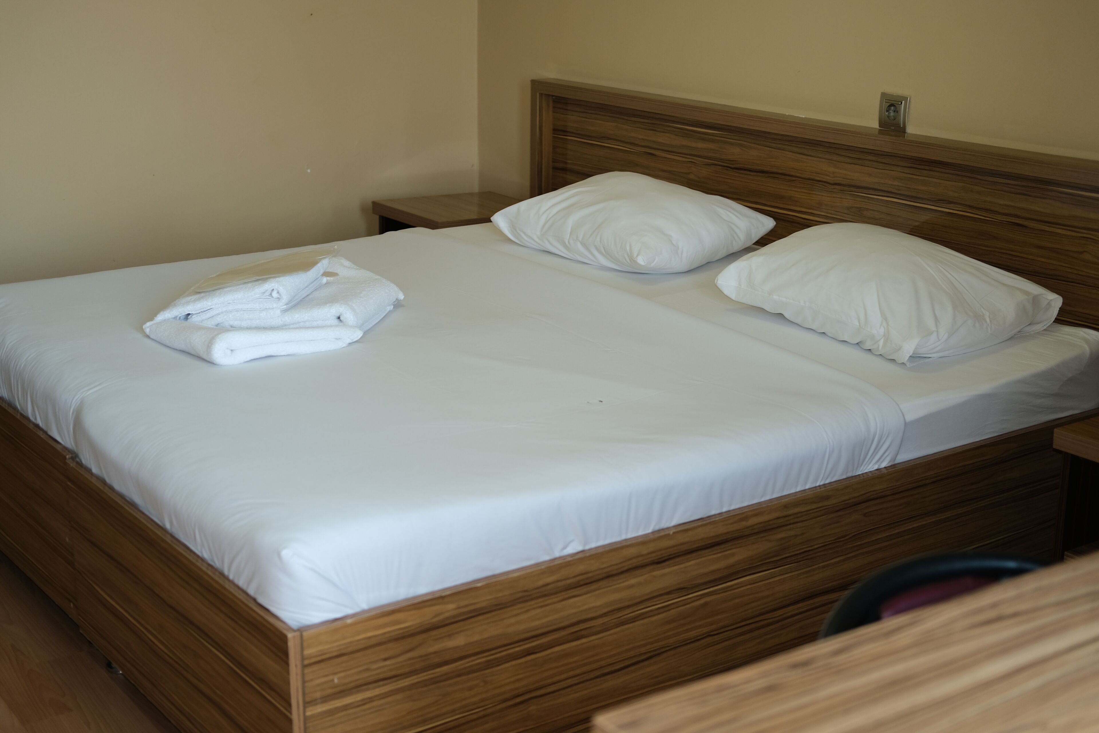 Un lit bien fait, avec du linge de lit blanc et des oreillers, une tête de lit en bois et une petite table de chevet avec une lampe.