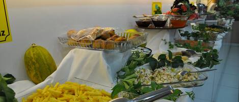 A buffet with various food items and a yellow sign on the wall.