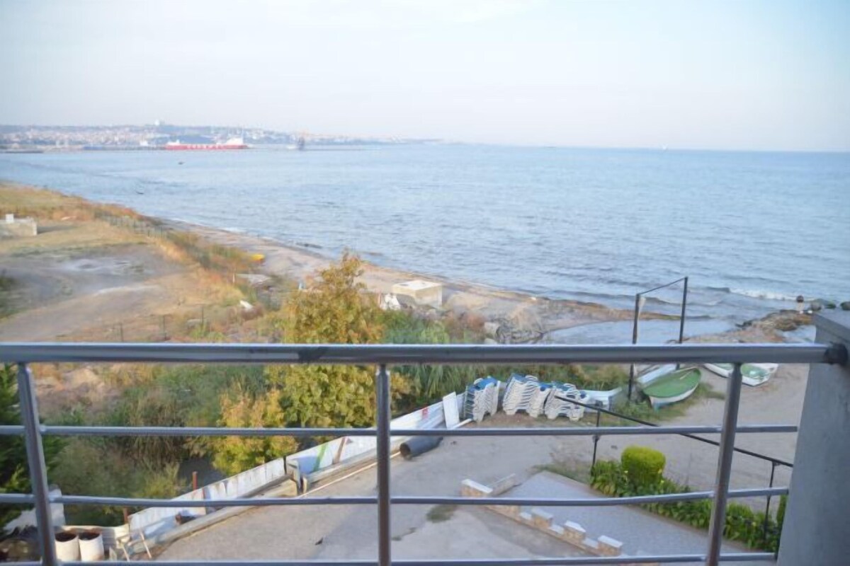 Vista desde un balcón con vista a una masa de agua, una costa lejana, materiales de construcción y un pequeño bote.