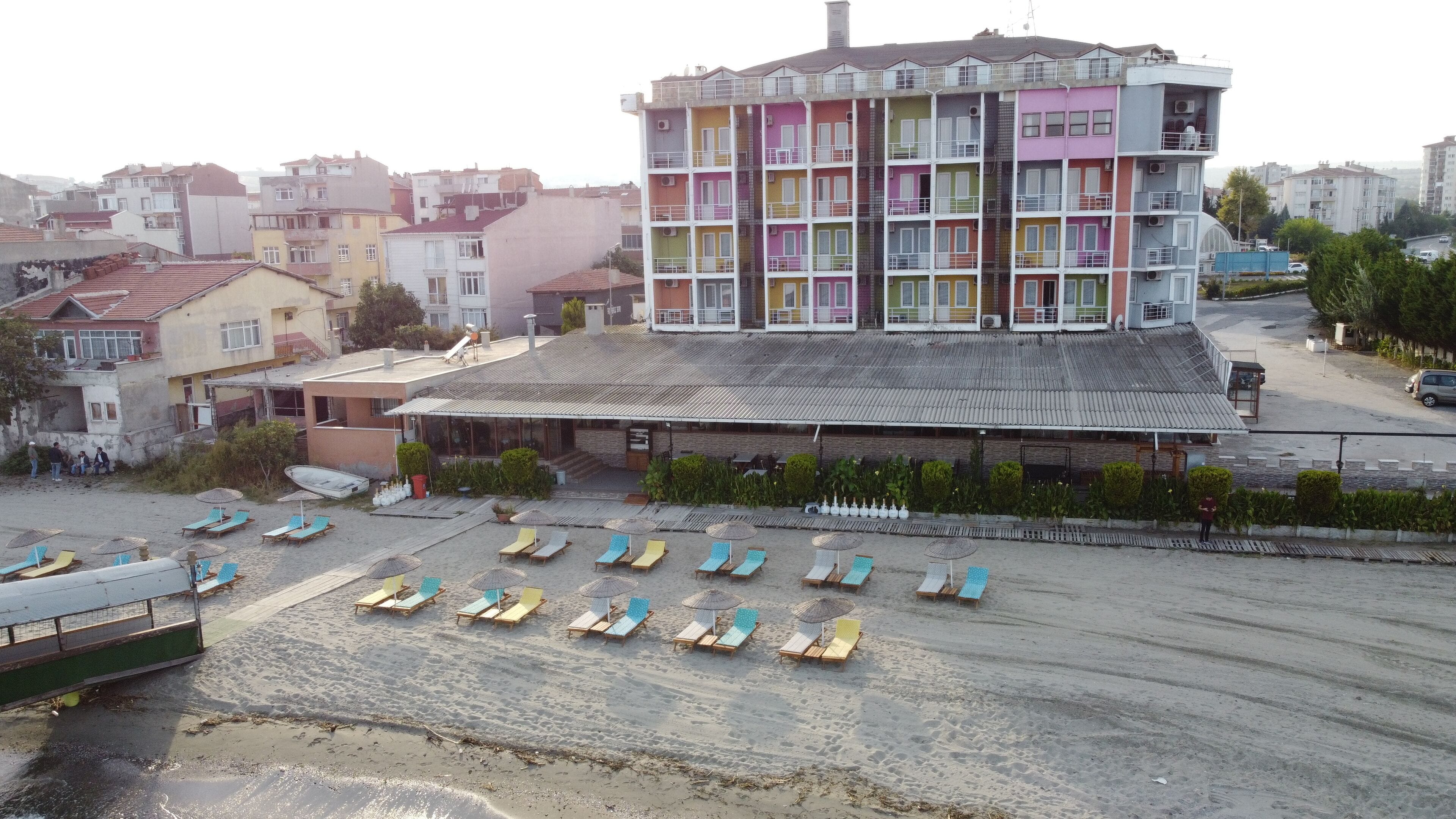 Un hotel de varios pisos con balcones de colores, un área de estar cubierta al aire libre y una playa de arena con sillas de sol.