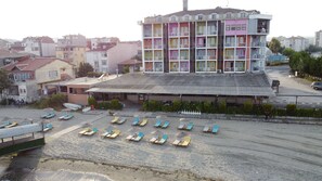 Un hotel de varios pisos con balcones de colores, un área de estar cubierta al aire libre y una playa de arena con sillas de sol.