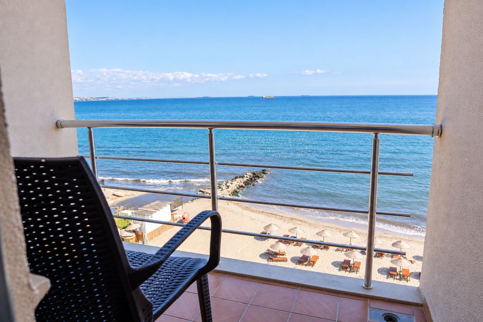 Un balcón con vista al mar, una silla y una mesa.