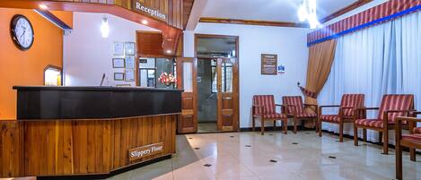 Zona de recepción con un mostrador de madera, un reloj y un cartel que indica la recepción.