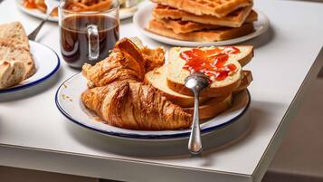 A breakfast setting with croissants, waffles, toast with jam, and a coffee mug on a table.