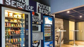 A vending machine with a variety of snacks and drinks, a microwave, and a service area with a sign for 'COOL SERVICE'. - ibis budget Caen Hérouville (Herouville-Saint-Clair)