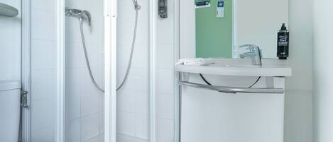 Un baño moderno con ducha de vidrio, inodoro blanco y lavamanos con espejo.