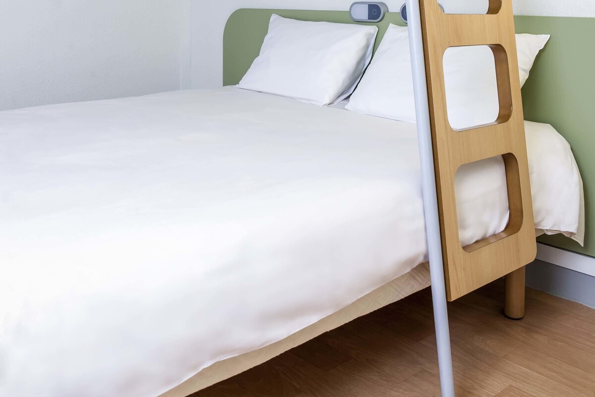 A single bed with a wooden frame and a green headboard, white bedding, and a bedside scale.
