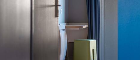 A narrow hallway with a small stool, a door, and a shelf against a wall.