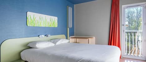 A bedroom with a bed, a bedside table, a wall-mounted light, and a window with curtains.