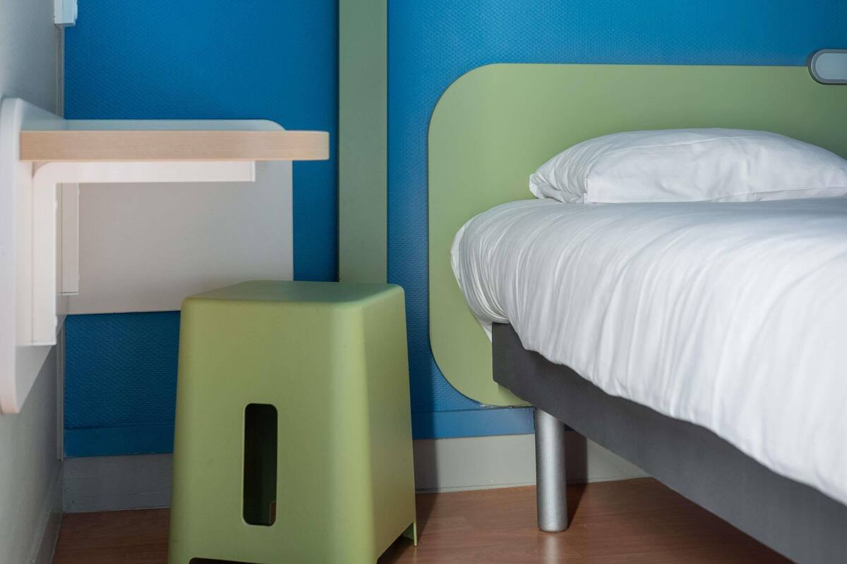 A room with a bed, a small stool, and a shelf unit.