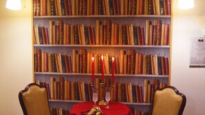 A room with a bookshelf filled with books, a table with a red tablecloth, two chairs, and two wall-mounted lamps. - Venice Lion Residence - Vespucci (Mestre)