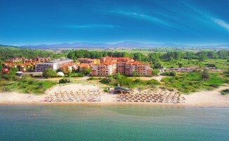A resort with multiple buildings, a beach with umbrellas and sun loungers, and a view of the surrounding landscape.