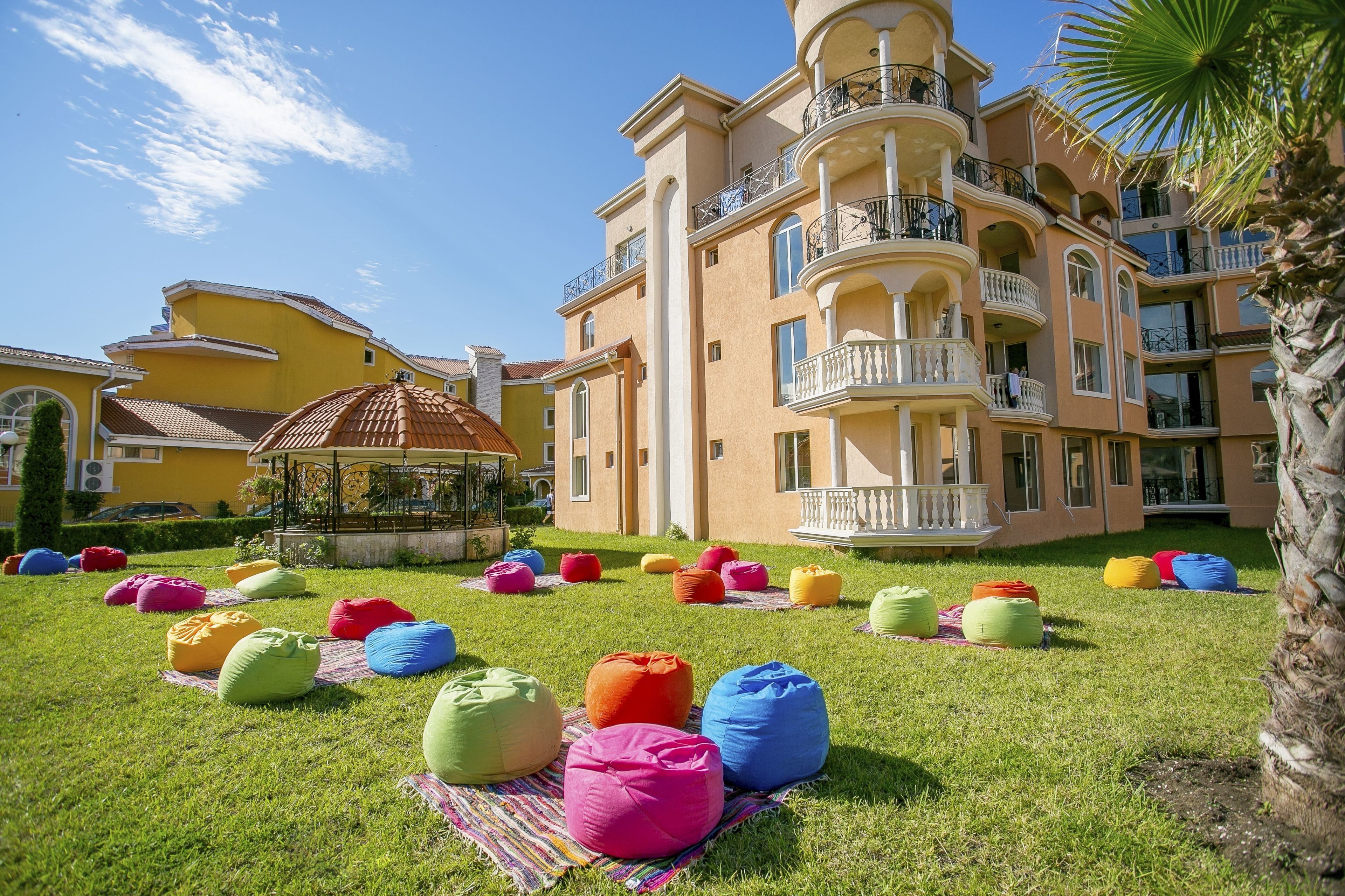 A large, multi-story building with balconies and a well-maintained lawn with colorful bean bags.