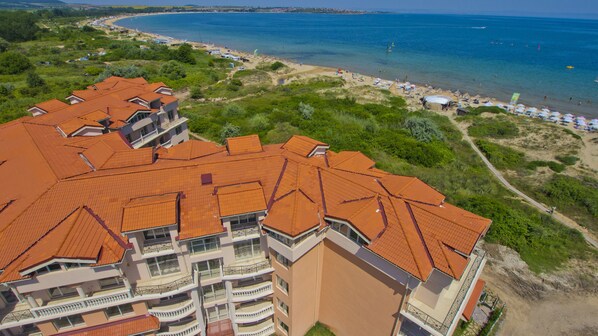 A multi-story building with a red-tiled roof, located near a beach with clear blue waters and sandy shores. - Hacienda Beach Resort (Sozopol)