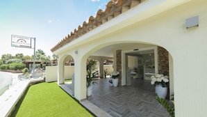 A modern building with a covered patio area, a sign for a restaurant, and a well-maintained lawn. - Suimi's Hotel (Villasimius)