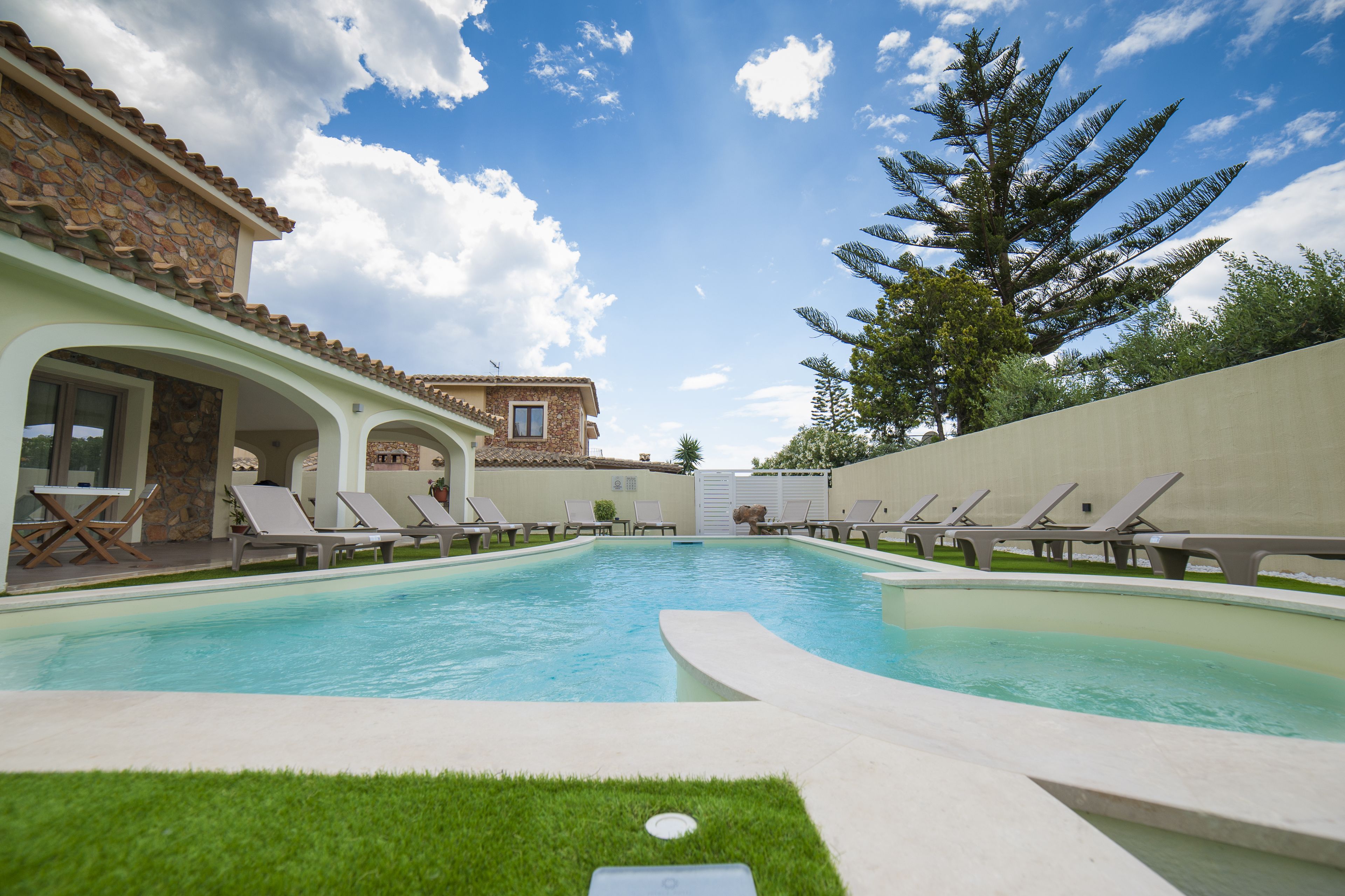 Una piscina con lettini e un edificio in pietra con tetto in tegole.