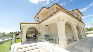 A hotel with a tiled roof, arched balconies, and a glass railing overlooking a landscaped area. - Suimi's Hotel (Villasimius)