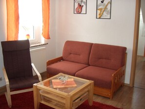A living room with a brown sofa, a wooden chair, a glass coffee table, and two framed pictures on the wall.