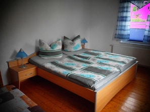 A bedroom with a wooden bed, two bedside tables, a night lamp, and a window with blinds.