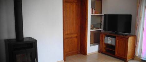 Una sala de estar con una estufa de leña, un televisor sobre un mueble de madera y una alfombra roja en el suelo.