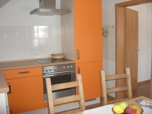 A kitchen with orange cabinets, a stove, and a wooden chair.