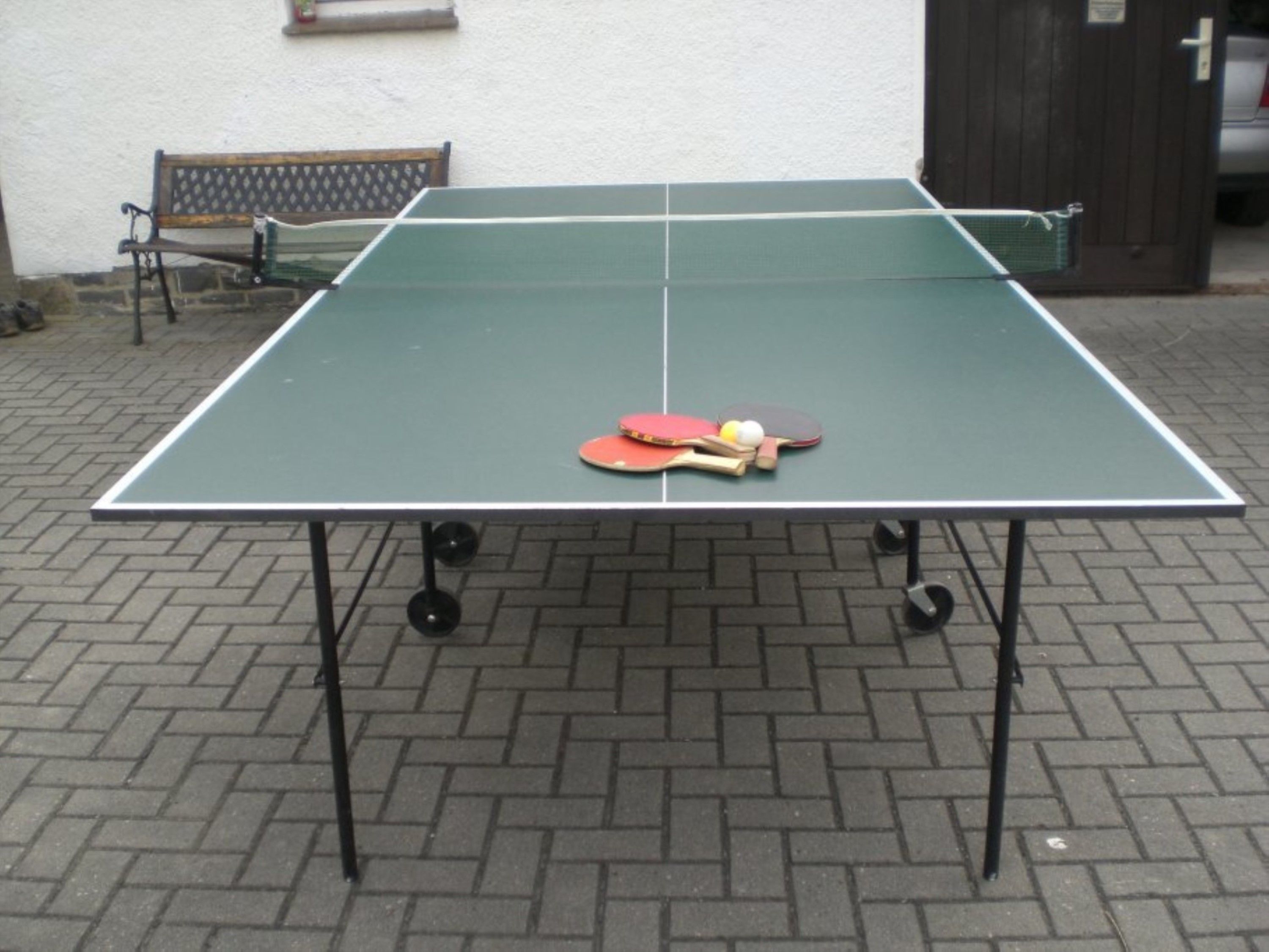 Ett bordtennisbord med racketar och bollar placerat på en trottoar av tegelstenar.