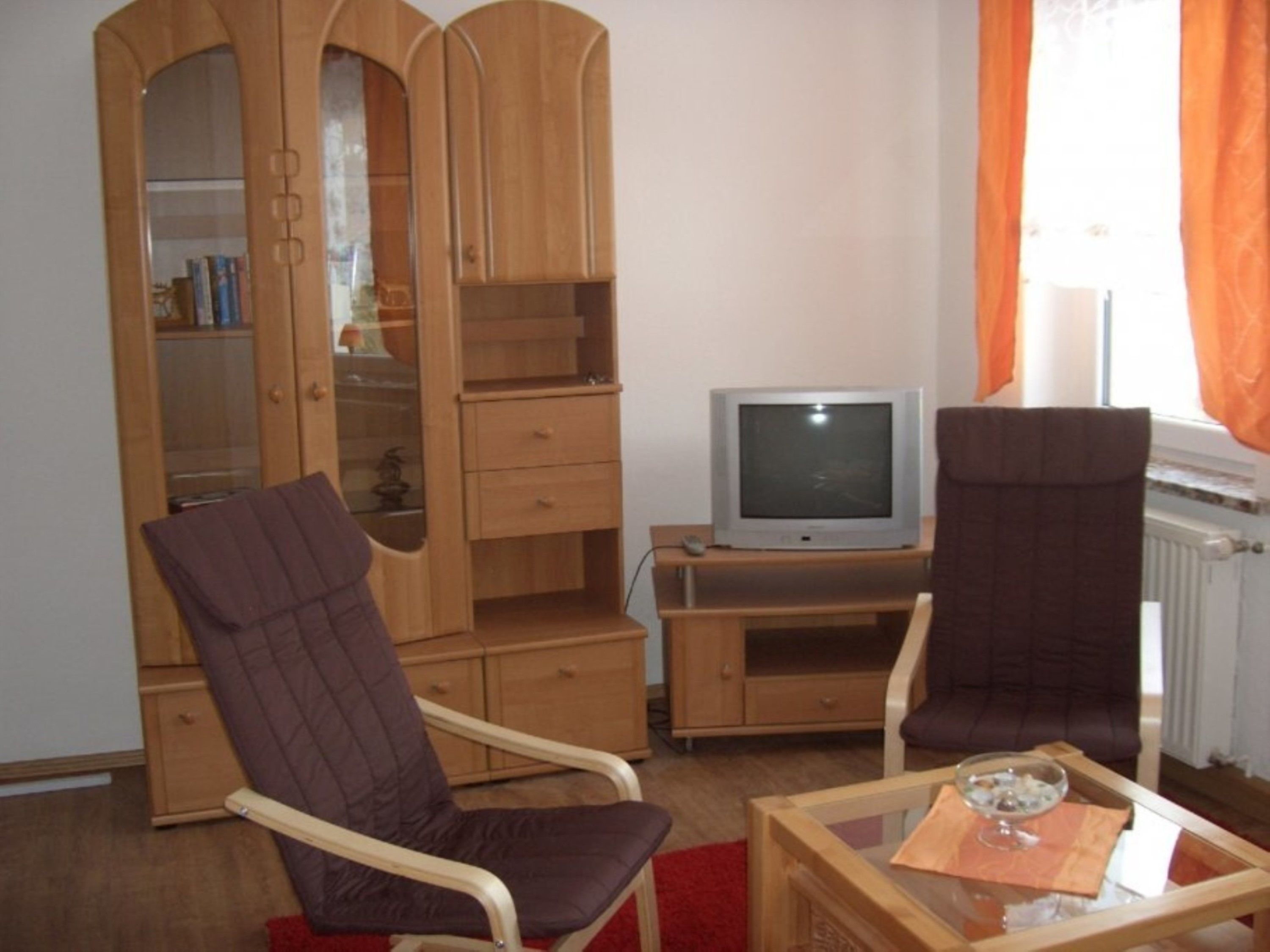 A living room with two armchairs, a television, a wooden cabinet, and a radiator.