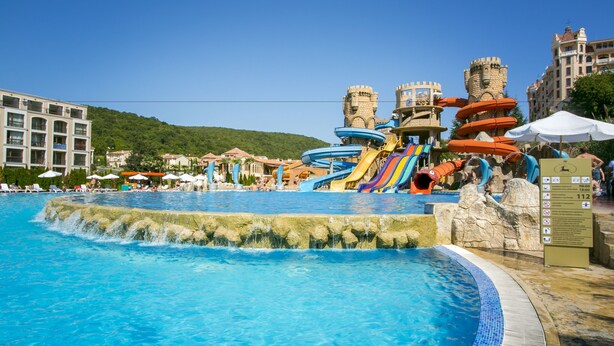 Una piscina con tobogán de agua y estructuras con temática de castillo.