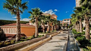 Un resort con un camino central bordeado por palmeras y una fuente de agua.