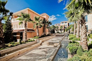 A hotel with a central courtyard, palm trees, and a tiled walkway.