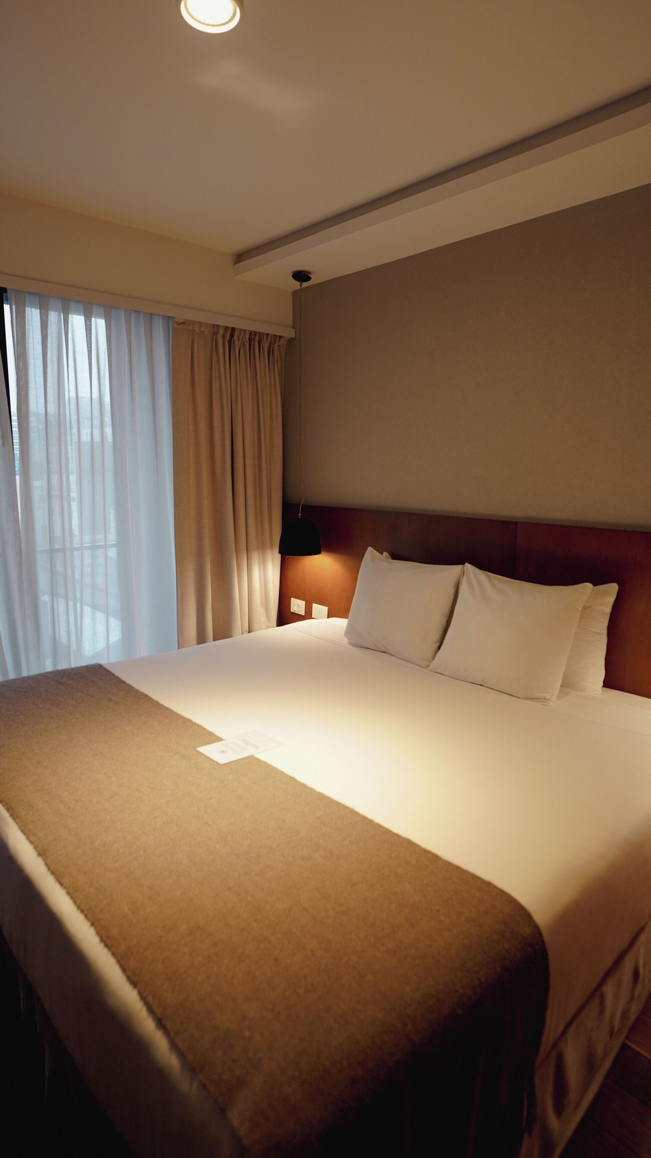 Une chambre d’hôtel avec un grand lit, une table de chevet, une lampe et une fenêtre avec des rideaux.
