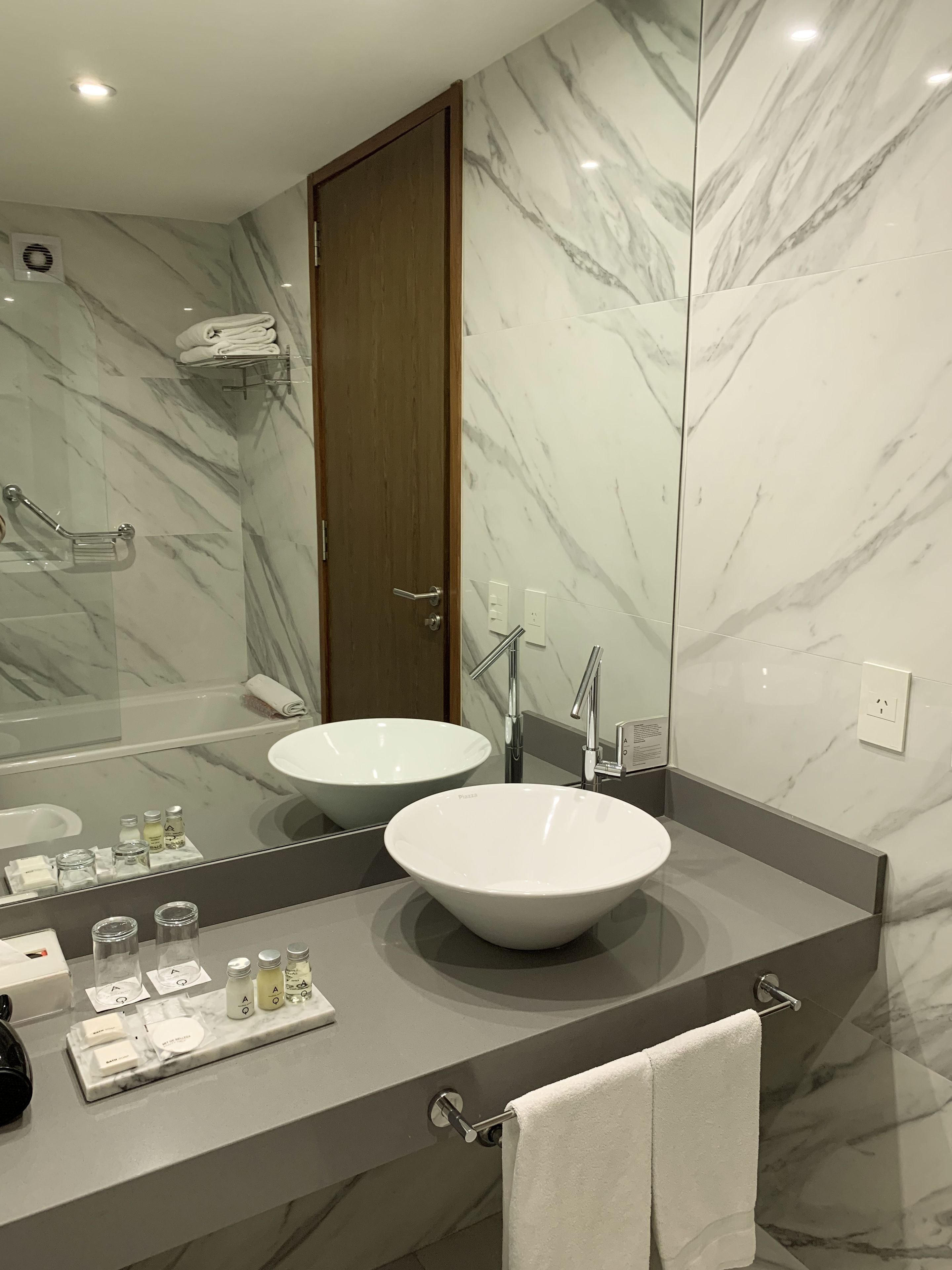 Un baño moderno con dos lavamanos, un espejo grande y paredes de mármol.
